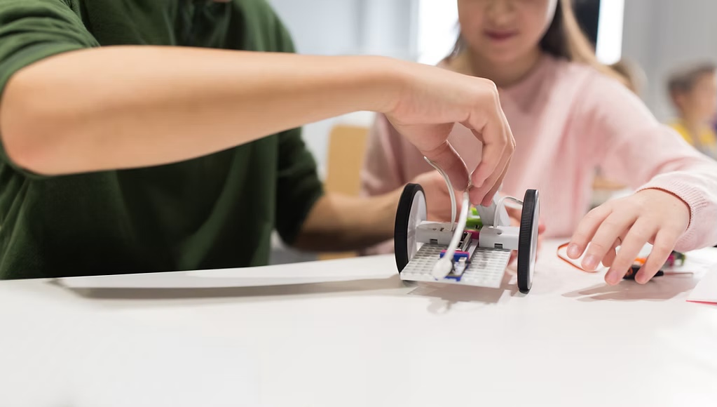 Bilim atölyesinde küçük tekerlekli bir robotu birleştiren katılımcılar