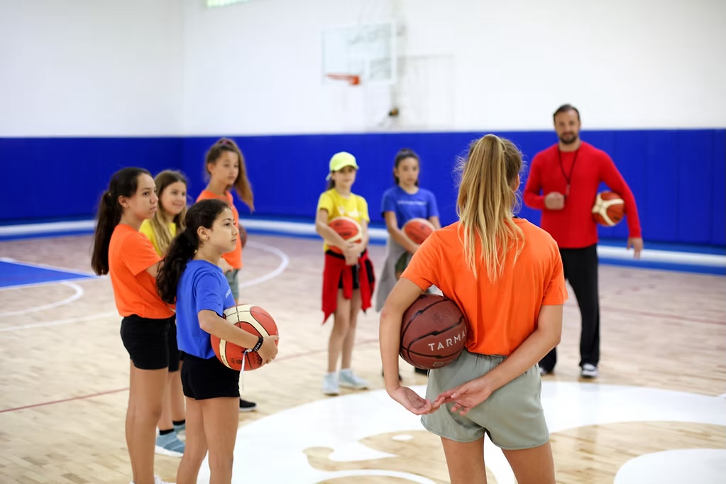 Spor salonunda eğitmenleriyle birlikte basketbol çalışan çocuklar