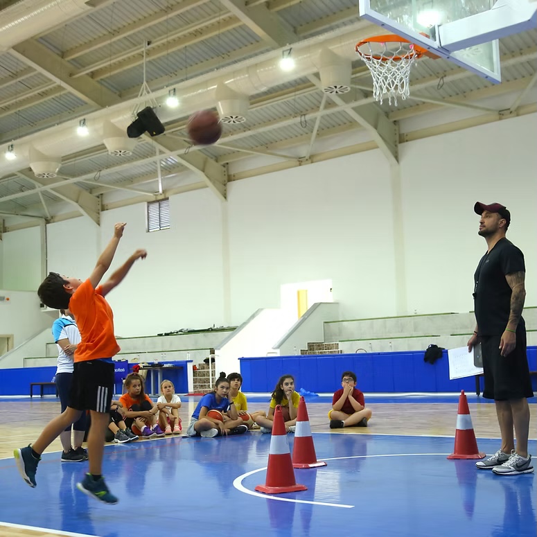 Antrenör eşliğinde basketbol atış çalışması yapan bir çocuk