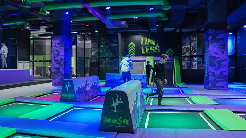 Playland oyun alanında mor ve yeşil minderlerle çevrili trambolinlerde oynayan ziyaretçiler
