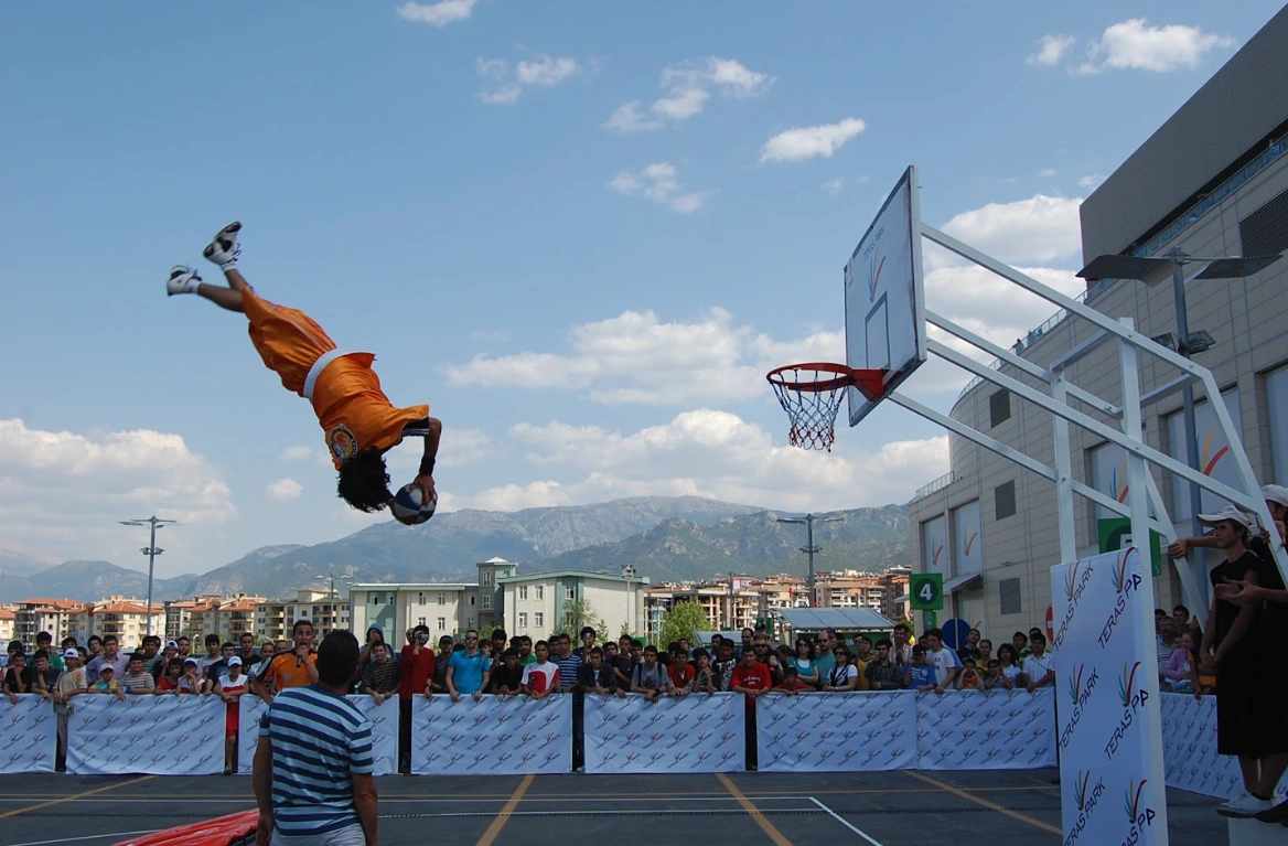 Açık hava basketbol gösterisinde, seyircilerin önünde topuyla havada takla atan bir sporcu