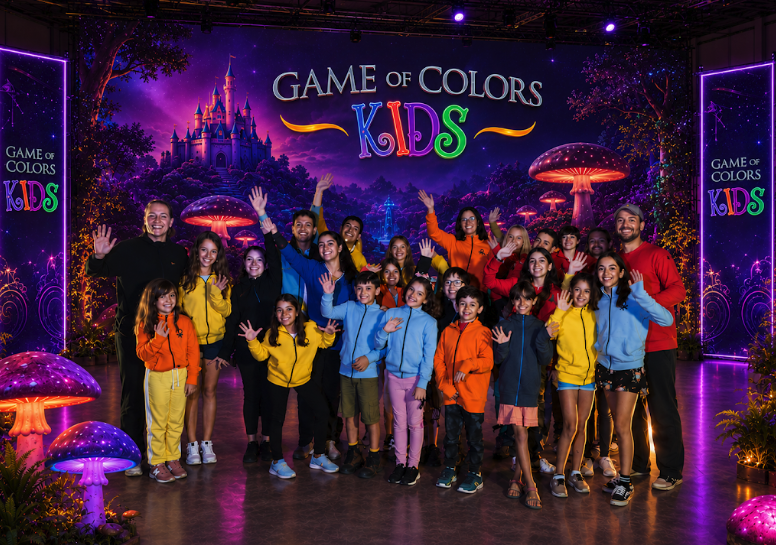 Renkli kıyafetli çocukların ve yetişkinlerin Game of Colors Kids dekoru önünde birlikte poz verdiği görsel