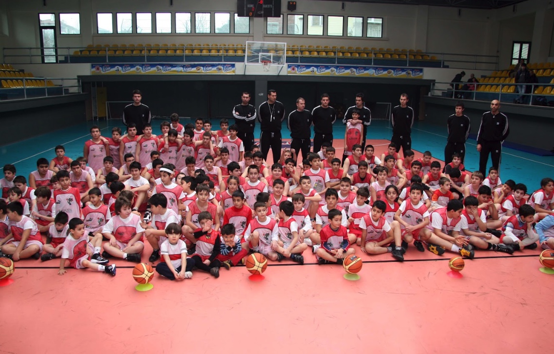 Pembe formalarıyla basketbol sahasında bir araya gelen çocuklar ve eğitmenler