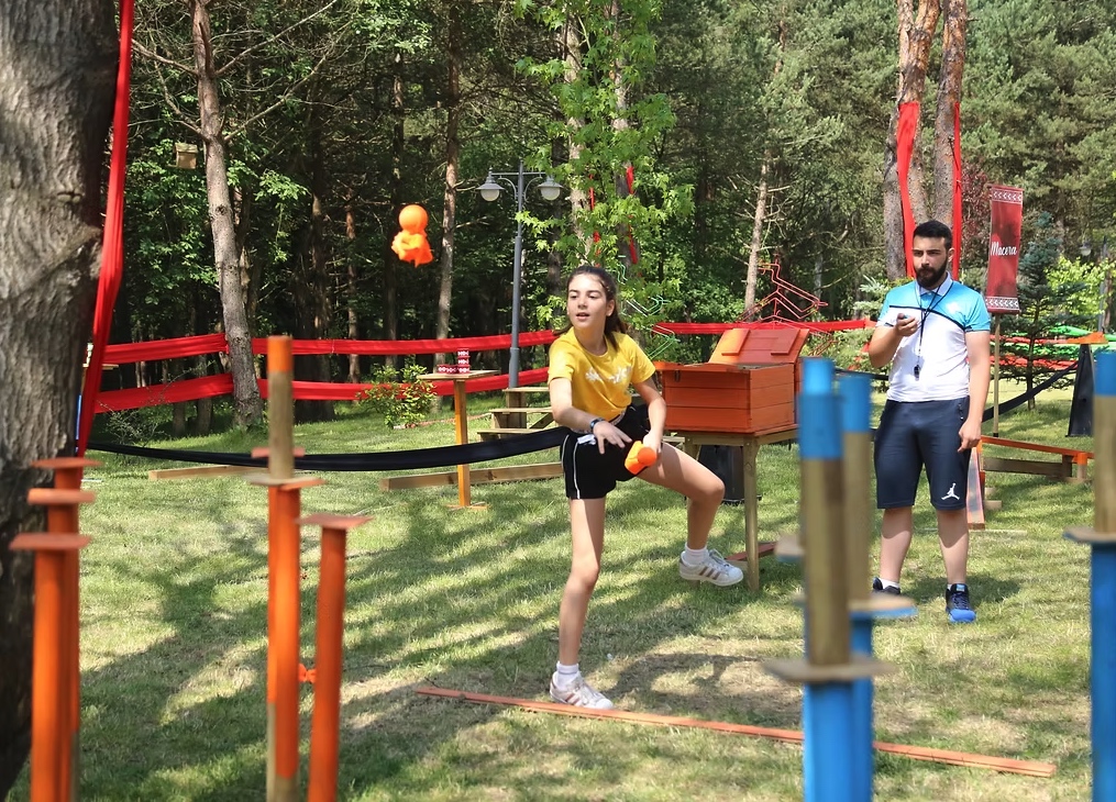 Açık hava oyun alanında eğitmen gözetiminde hedef atma etkinliğine katılan çocuk