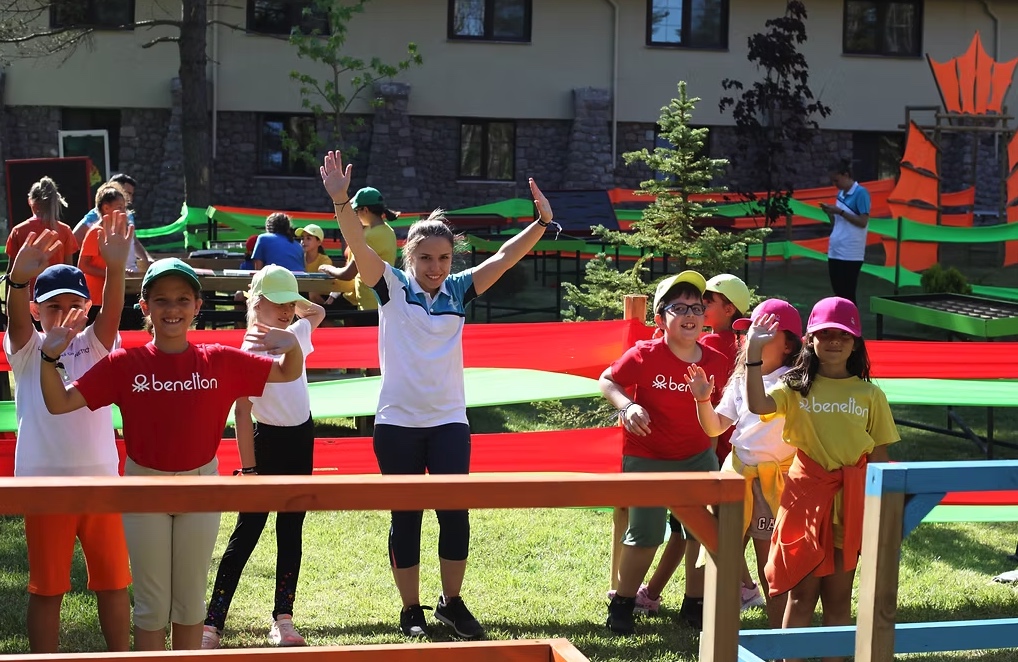 Renkli açık hava parkurunda eğitmenleriyle birlikte el sallayan çocuklar
