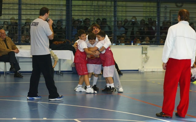 Basketbol sahasında kırmızı beyaz formalı çocukların bir sporcuya sarıldığı hatıra anı — temsili arşiv görseli