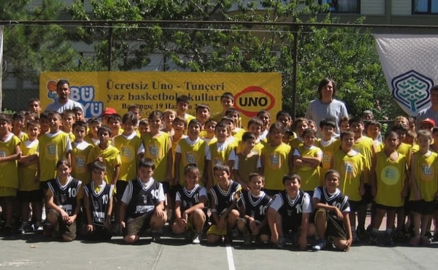 Ücretsiz Uno–Tunçeri yaz basketbol okulları pankartı önünde sarı ve siyah formalarıyla bir araya gelen çocuklar ve eğitmenler
